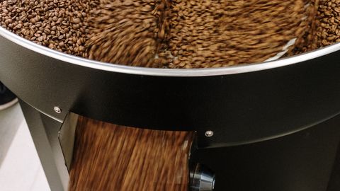 Close-up of coffee beans being roasted in an industrial machine, emphasizing motion and production.