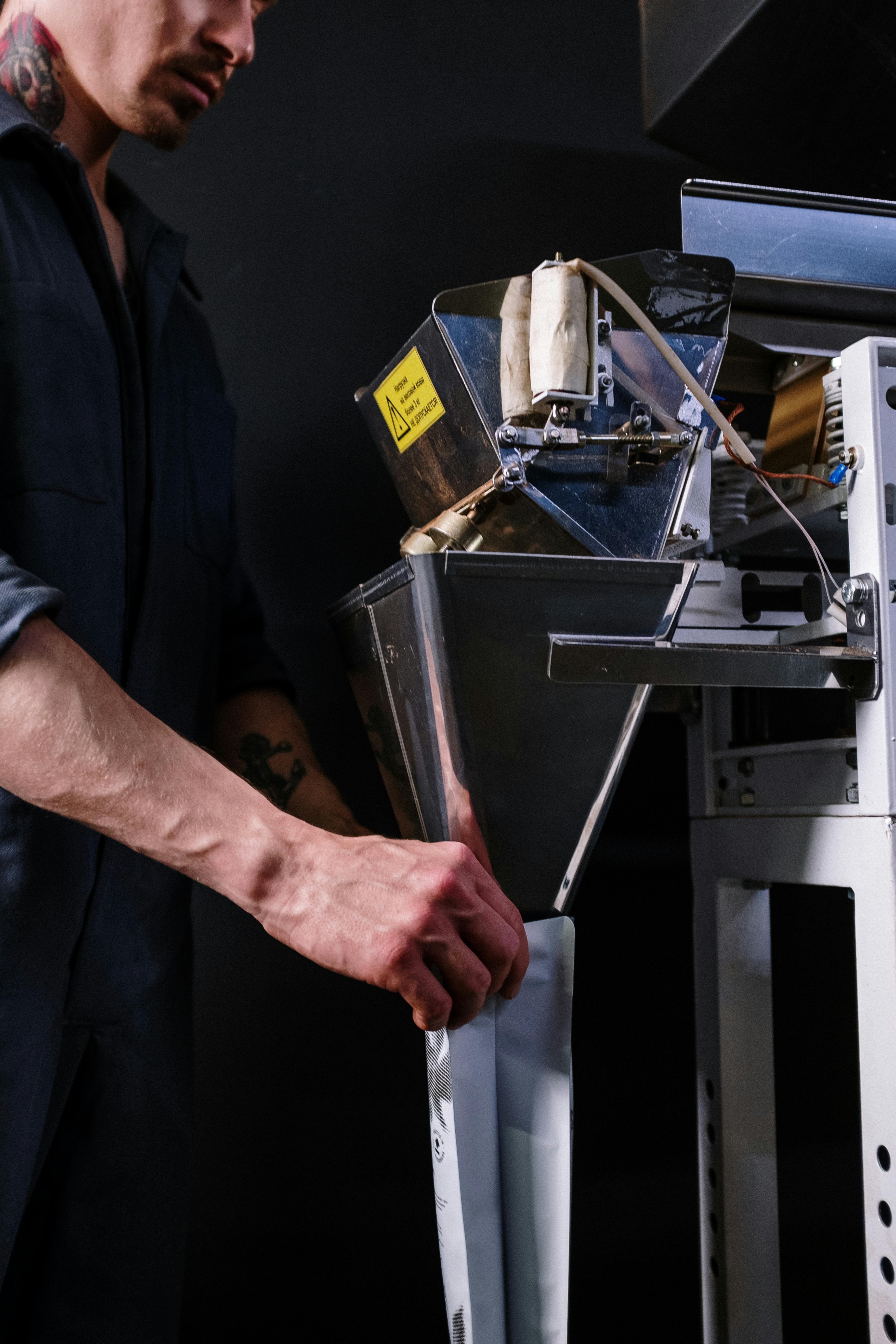 Man in uniform operating a coffee packaging machine in a modern workspace.