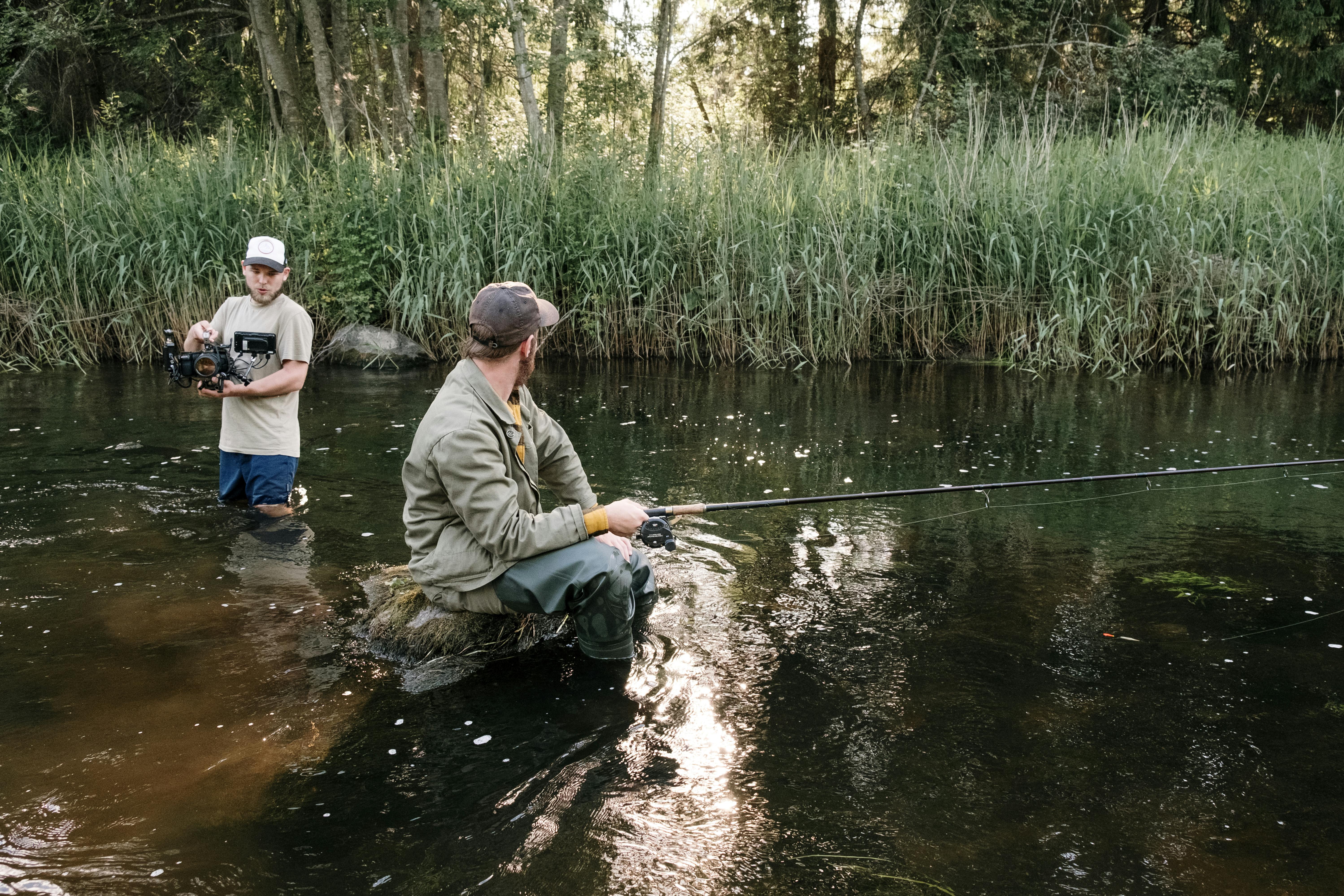 A filmmaker captures a fisherman doing his craft in a serene river setting, surrounded by lush nature.