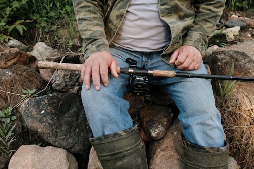 Person in Green and Brown Camouflage Jacket and Blue Denim Jeans Holding Black and Brown Rifle