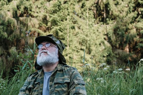Free Elderly man in camouflage outdoors, surrounded by greenery, enjoying nature. Stock Photo