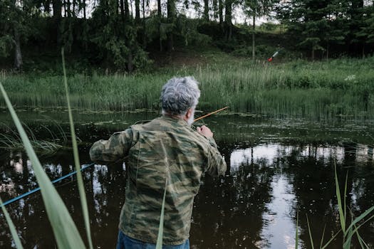 一名身穿迷彩服的男子在宁静的森林湖边垂钓，水中倒影重重