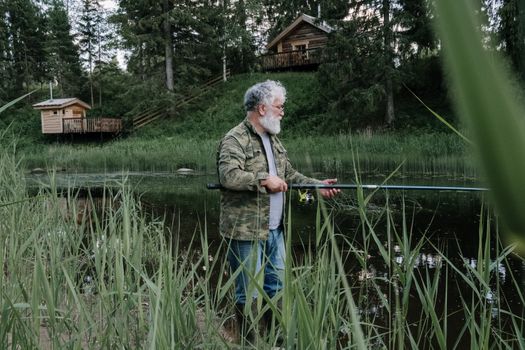 一名留着胡子的男子在乡村小屋附近的宁静森林湖边钓鱼