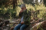 一位年长男子在户外钓鱼，在大自然和绿色植物的环绕中放松身心