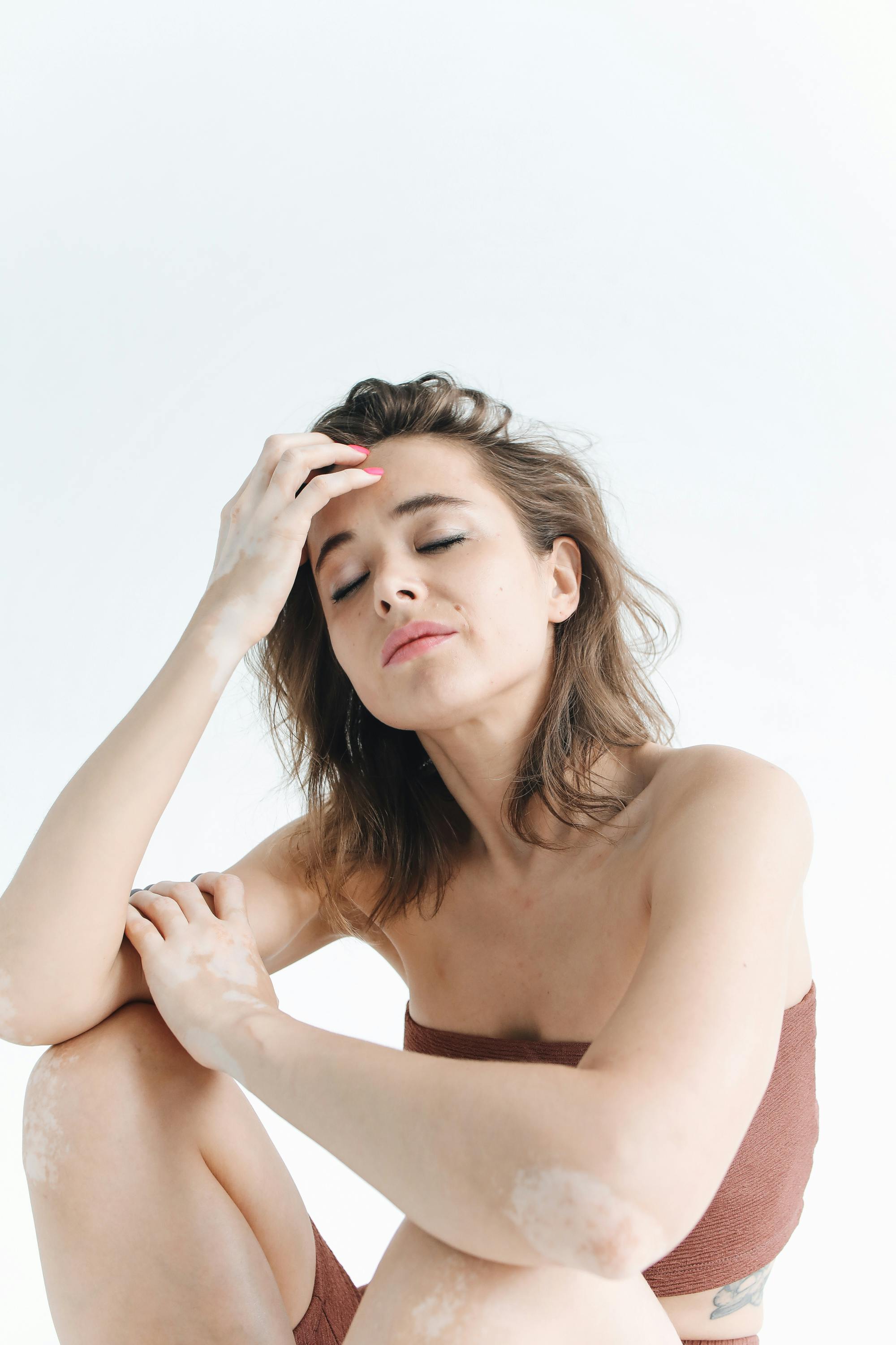 这幅肖像画描绘了一位闭目扶额、背景纯白的女性，整体氛围宁静平和