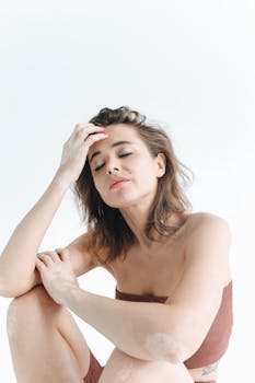 这幅肖像画描绘了一位闭目扶额、背景纯白的女性，整体氛围宁静平和