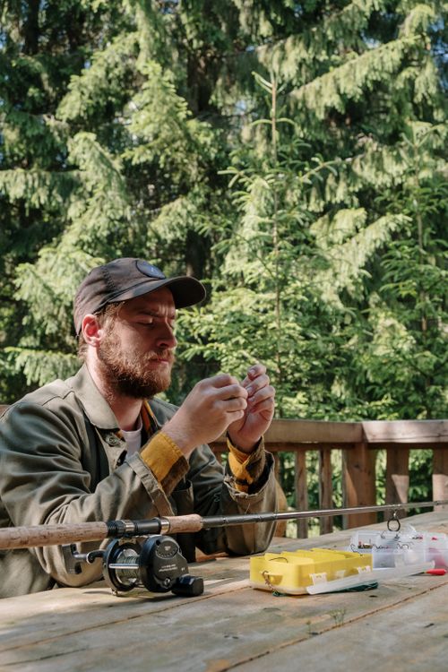 Free A bearded man setting up fishing gear on a wooden table in a forested area. Stock Photo