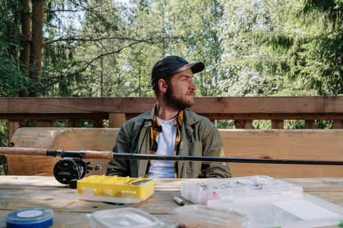 Free Man with beard sitting outdoors with fishing equipment, capturing nature's essence. Stock Photo