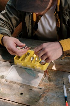 A man organizing fishing tackle on a wooden surface outdoors.
