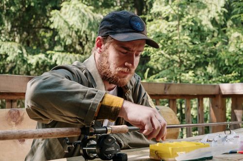 Free A focused bearded man setting up fishing gear on a sunny terrace, surrounded by nature. Stock Photo
