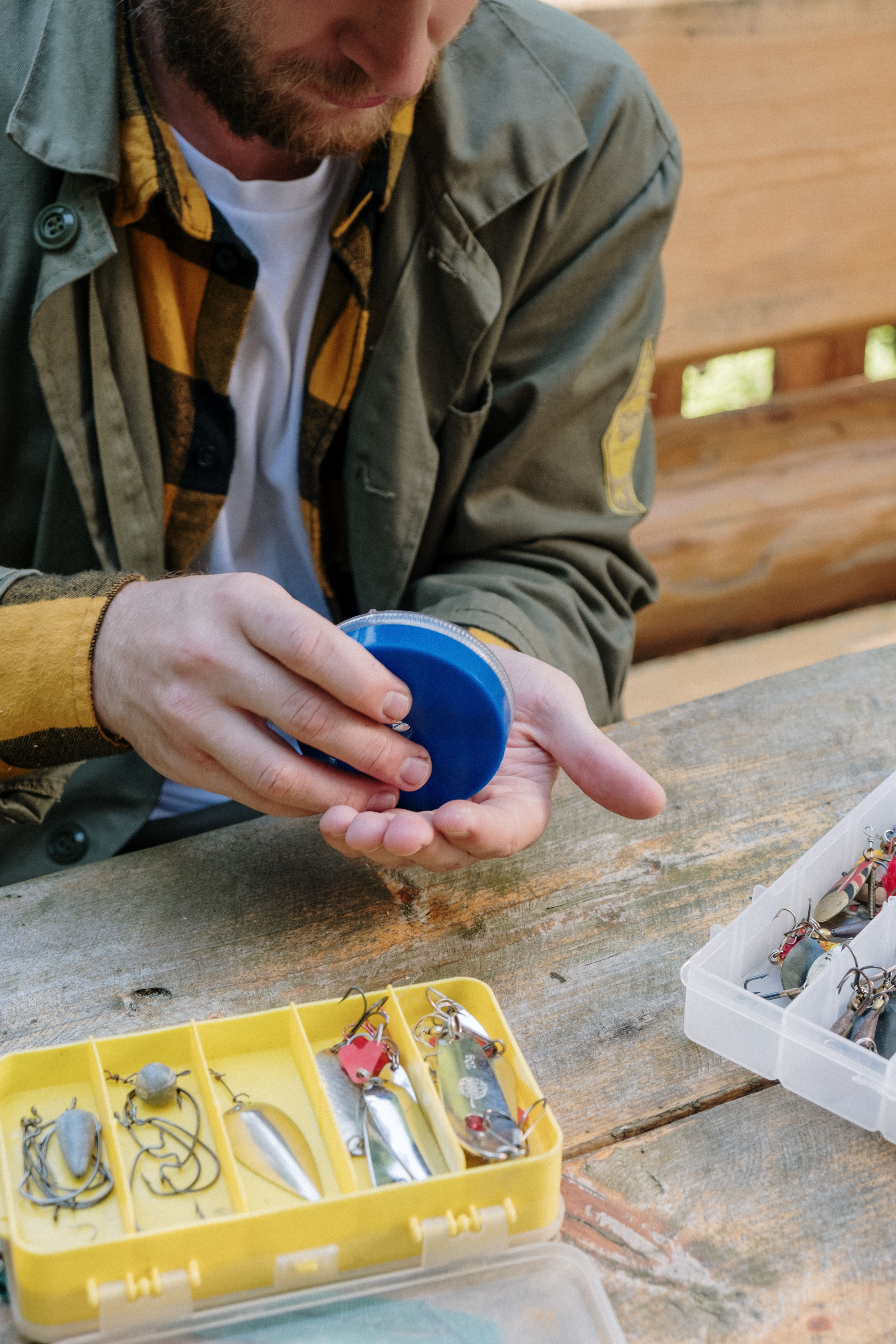 A fisherman organizing fishing lures and gear on a rustic wooden table outdoors, ensuring everything is ready for the trip.