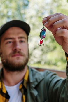 A bearded man holding a colorful fishing lure, showcasing outdoor fishing gear in natural daylight.