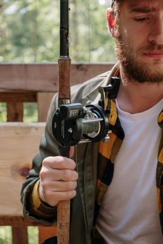 A bearded man holds a fishing rod with concentrated expression outdoors.