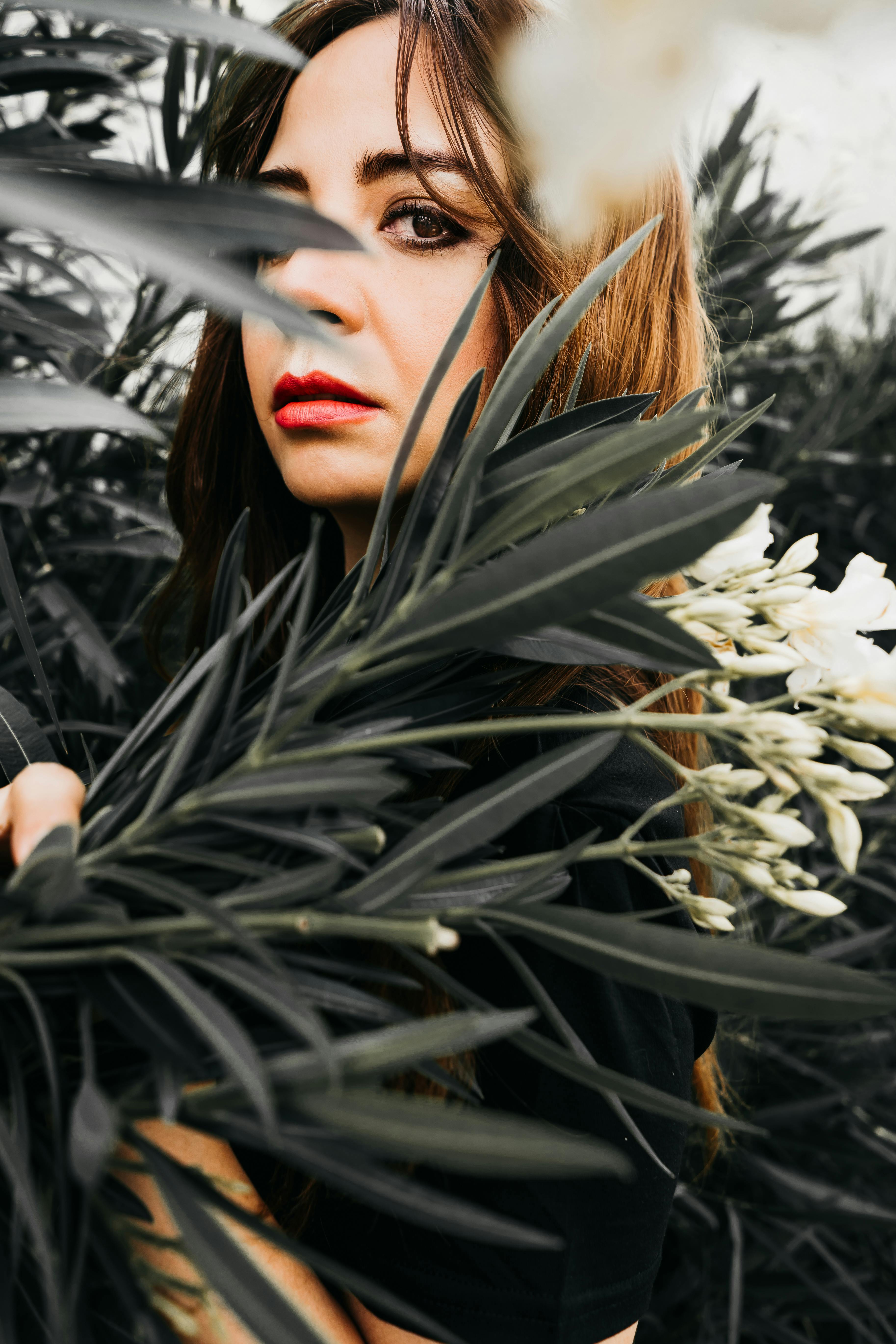 Striking portrait of a brunette woman surrounded by lush oleander leaves and flowers in Zapopan, Mexico.