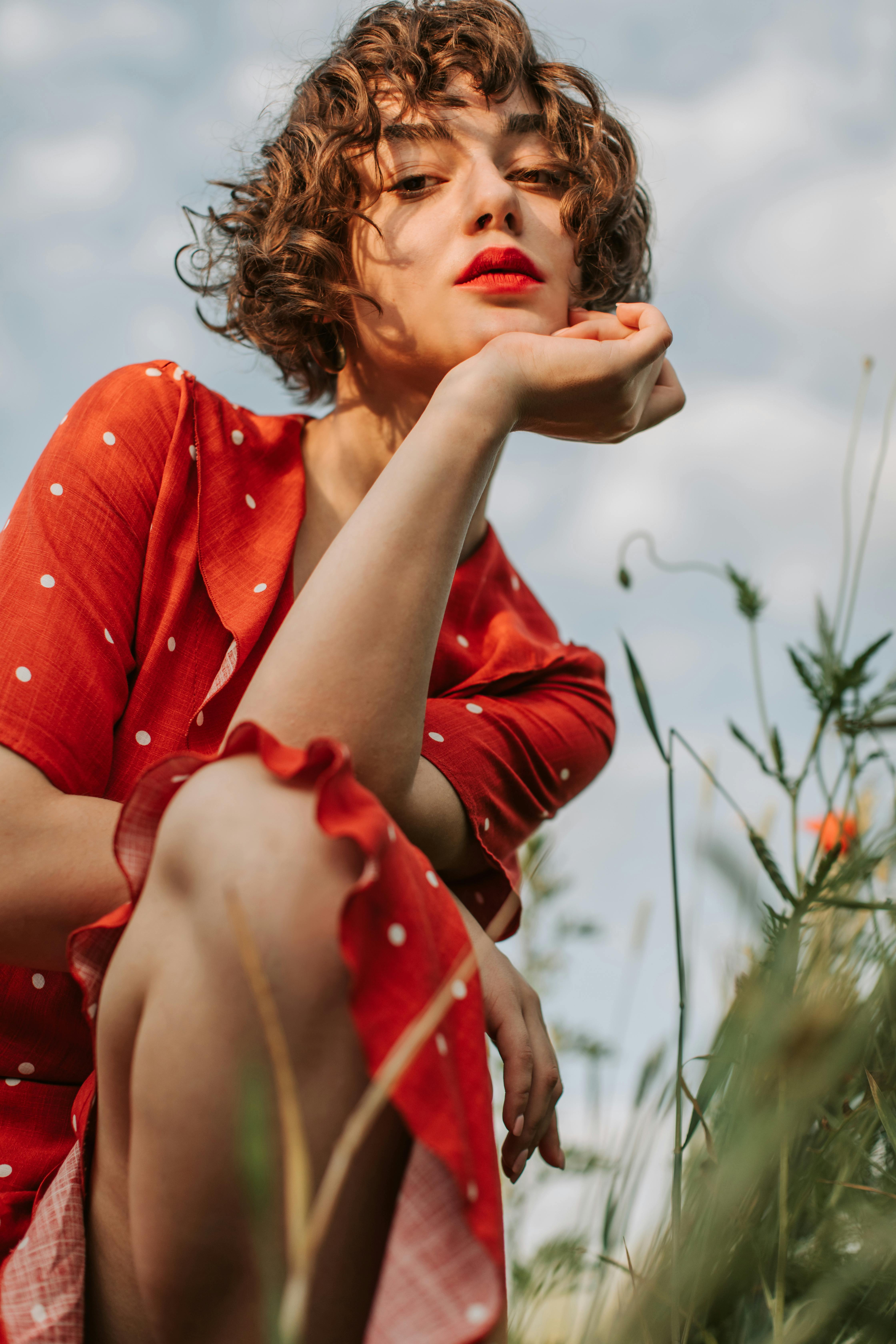 一位卷发的时尚女士身着充满活力的红色连衣裙，在户外摆姿，更显美丽