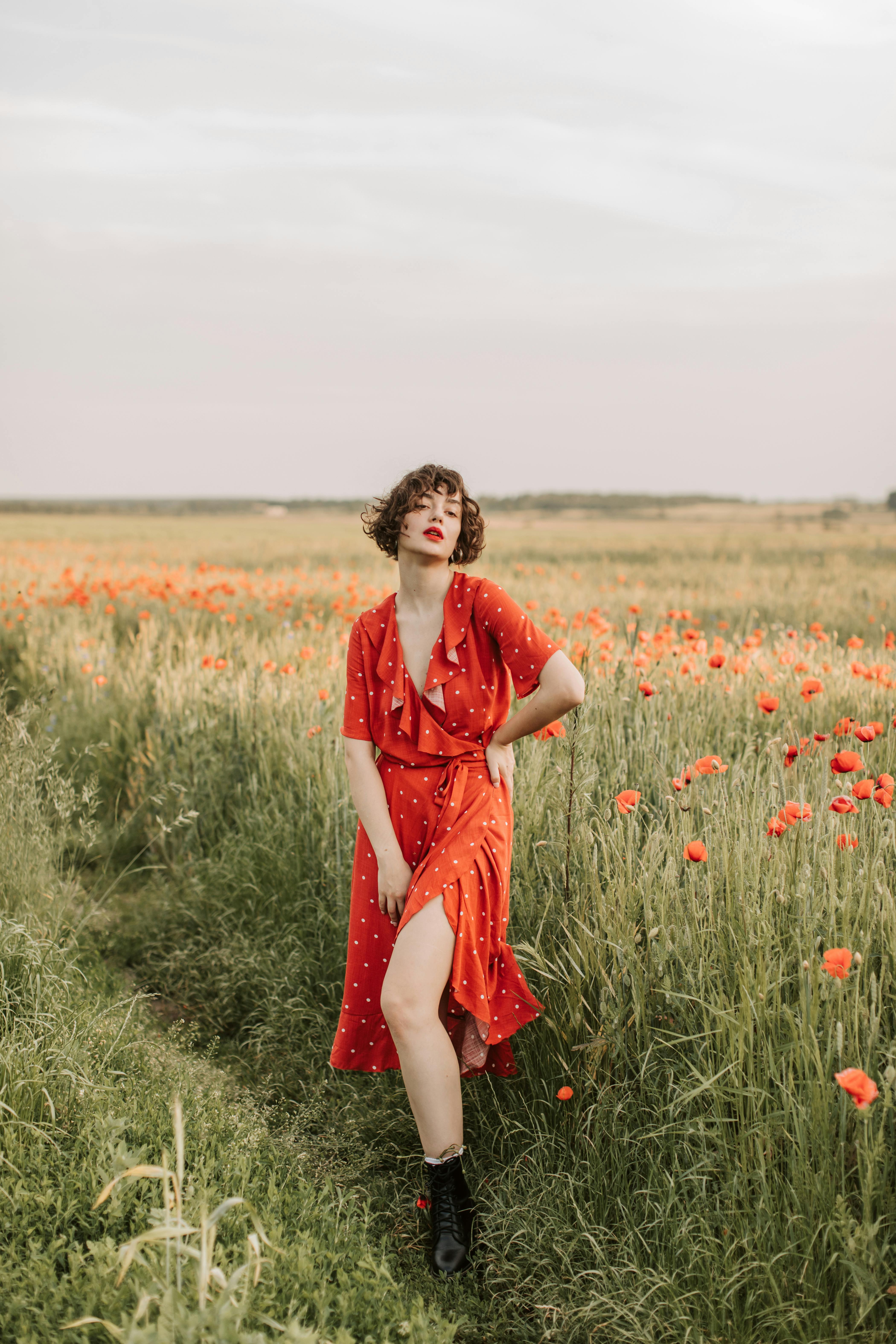 Woman in a red dress standing in a poppy field, conveying summer elegance.