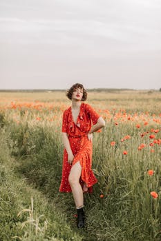 Woman in a red dress standing in a poppy field, conveying summer elegance.