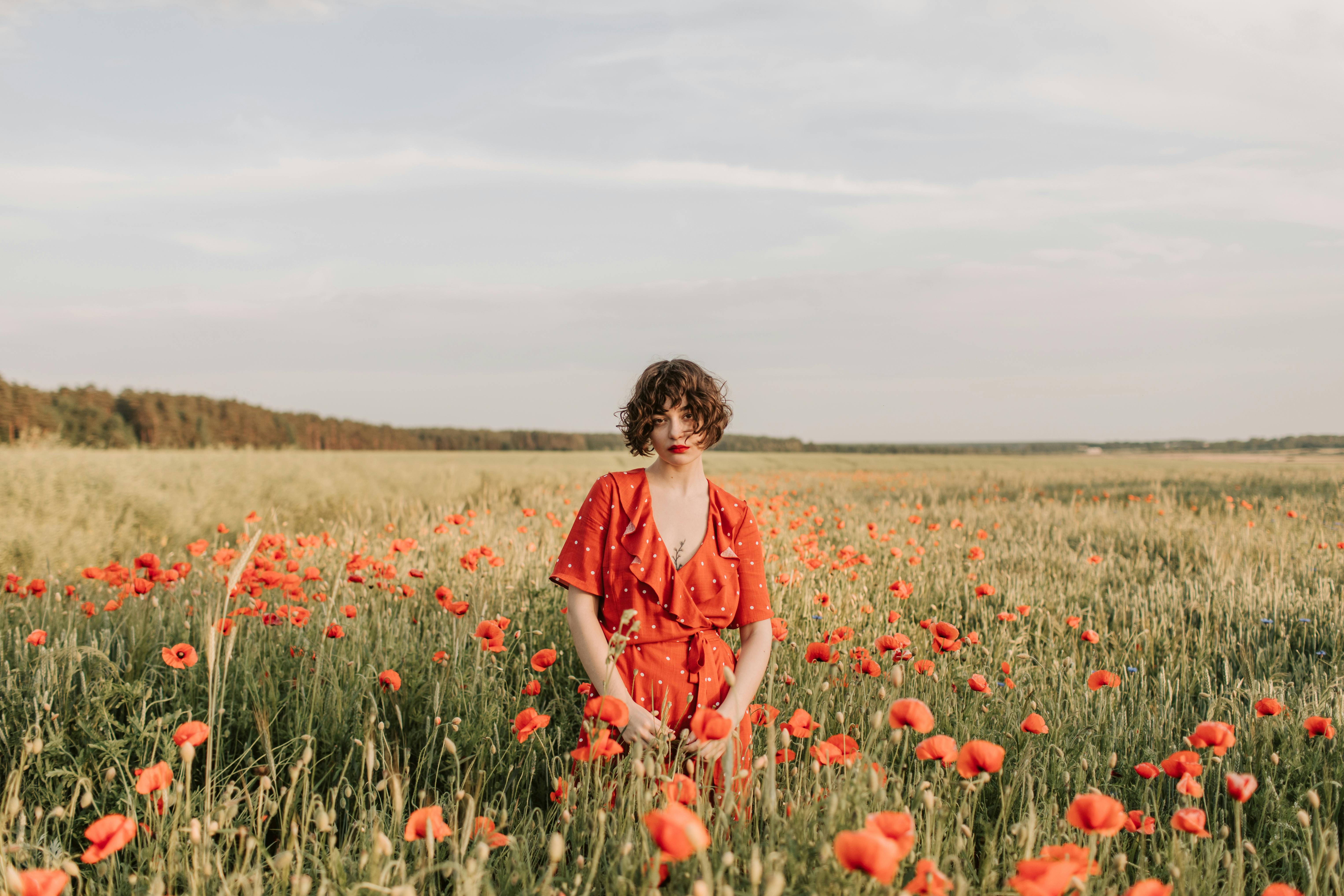 晴朗的天空下，一名身穿红色连衣裙的女子优雅地站在充满活力的罂粟田里