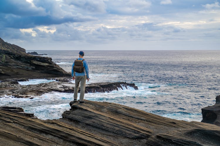 Man With Backpack Looking At Rocky Coast