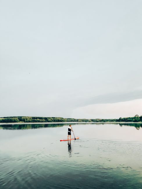A lone person enjoying standup paddleboarding on a calm and peaceful lake.