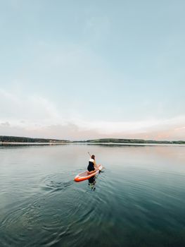 A woman paddleboards on a tranquil lake during sunset, embracing adventure and nature's beauty.
