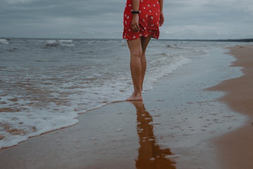 Free Woman in Red and White Floral Dress Standing on Beach Stock Photo