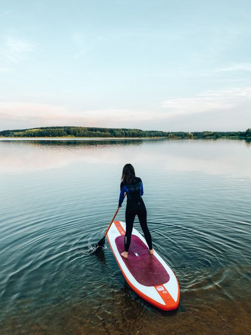 Free A woman paddleboards alone on a tranquil lake surrounded by nature during sunset. Stock Photo