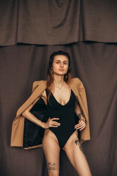 Stylish woman in brown blazer and swimsuit with tattoos in fashion photoshoot.