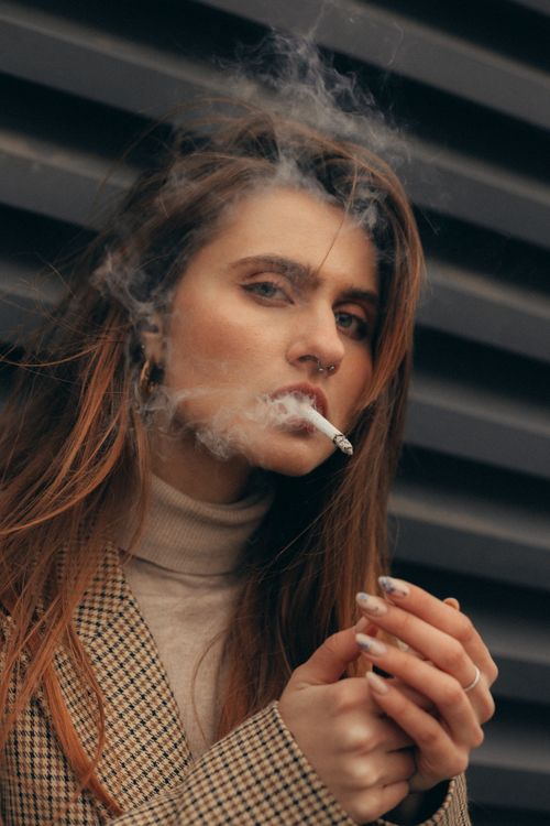 Free Woman in checkered coat smoking a cigarette against a textured background. Stock Photo