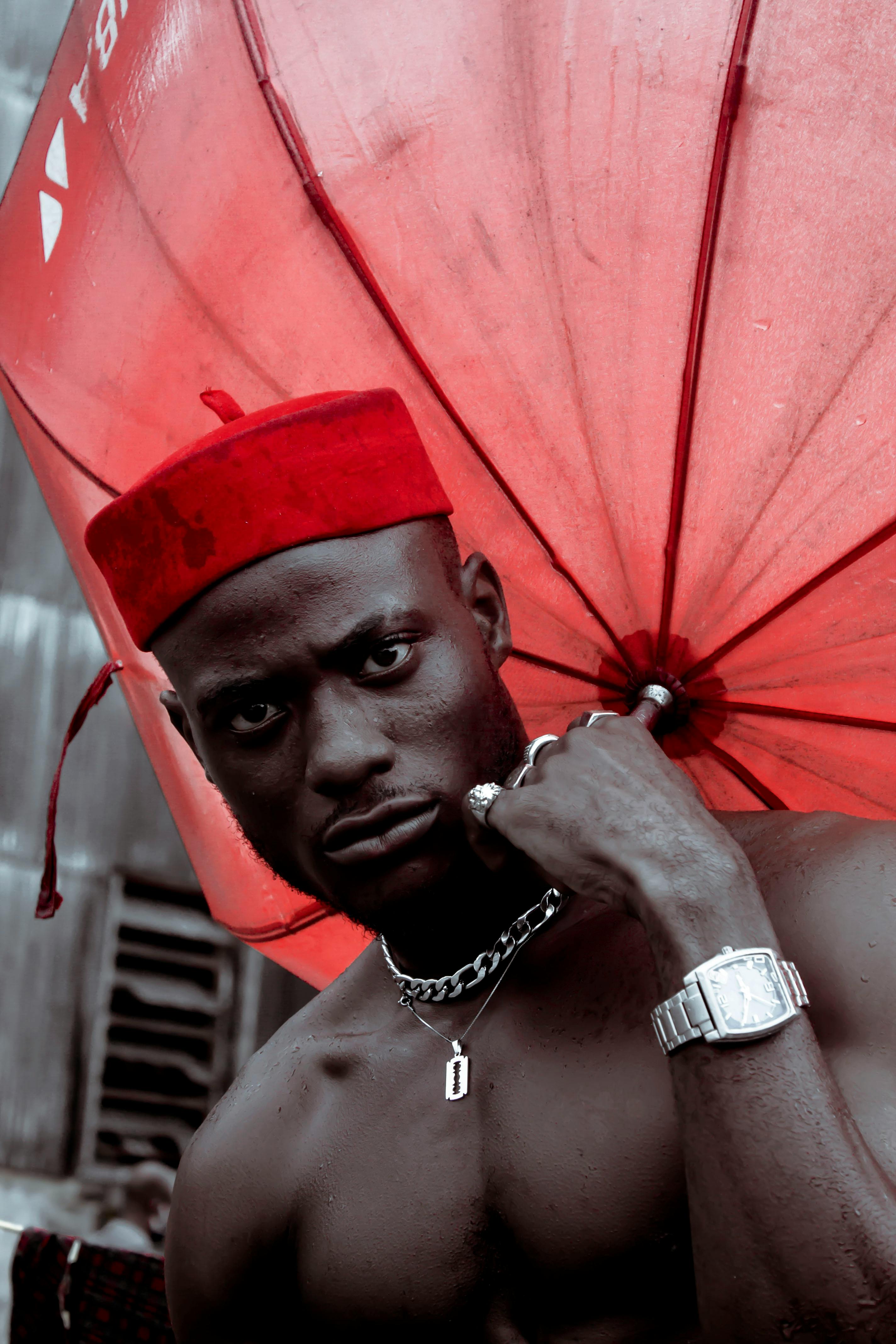 Shirtless man with a red umbrella and hat, striking expression