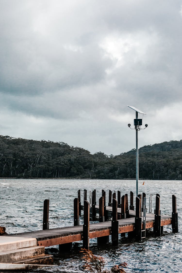 Old Dock On Sea Against Mountain Under Cloudy Sky