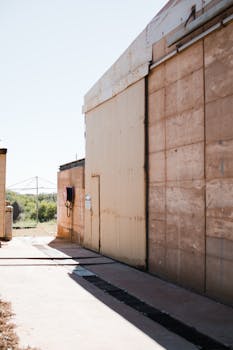 Exterior of big warehouse building with shabby concrete and metal walls in fenced area