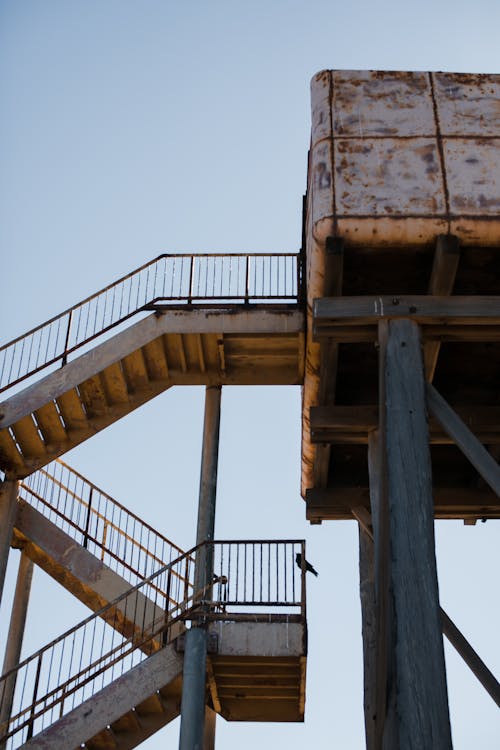 Low angle of tall aged observation tower on tall poles with rusty staircase against clear sky