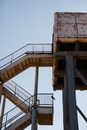 Low angle of tall aged observation tower on tall poles with rusty staircase against clear sky