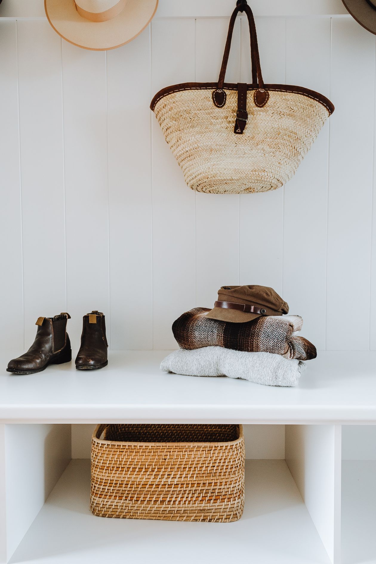 White hallway bench with a woven basket in the cubby, boots and hats on top