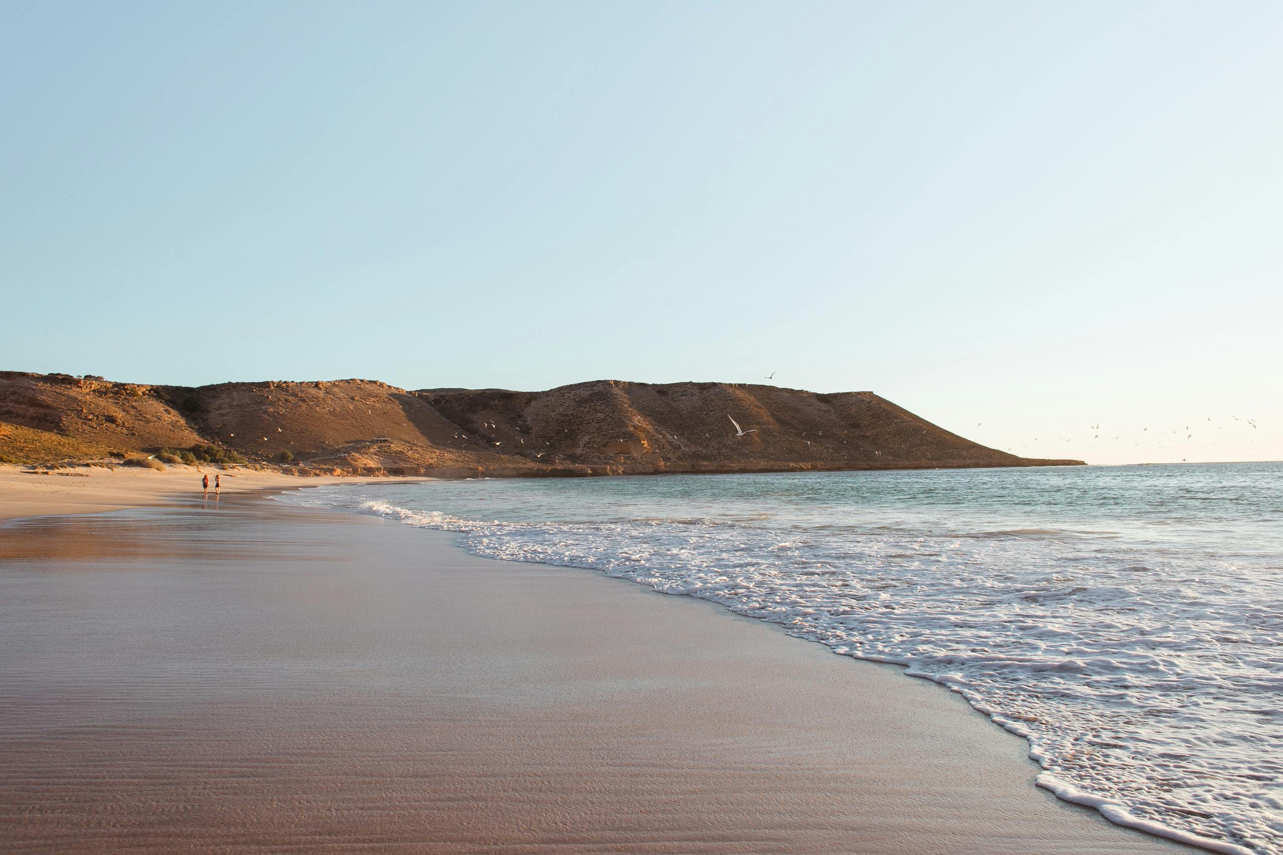 Sandy beach near calm sea with mountains · Free Stock Photo