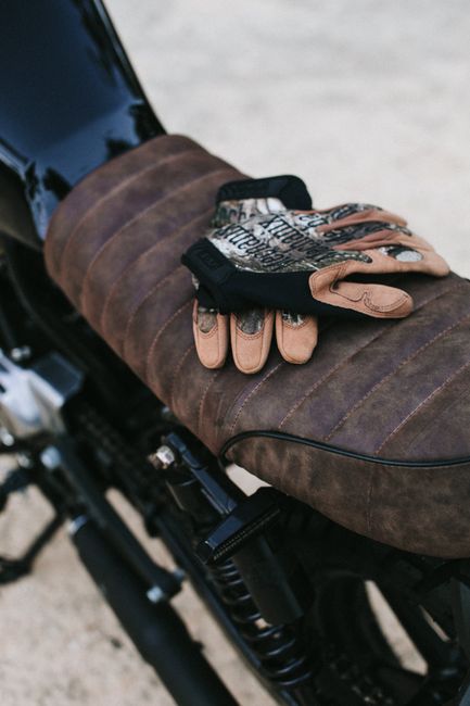 Black motorcycle with gloves on seat parked on sandy ground in summer day outside
