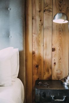 Interior of bedroom with bed near lamp and glasses located on nightstand near wooden wall