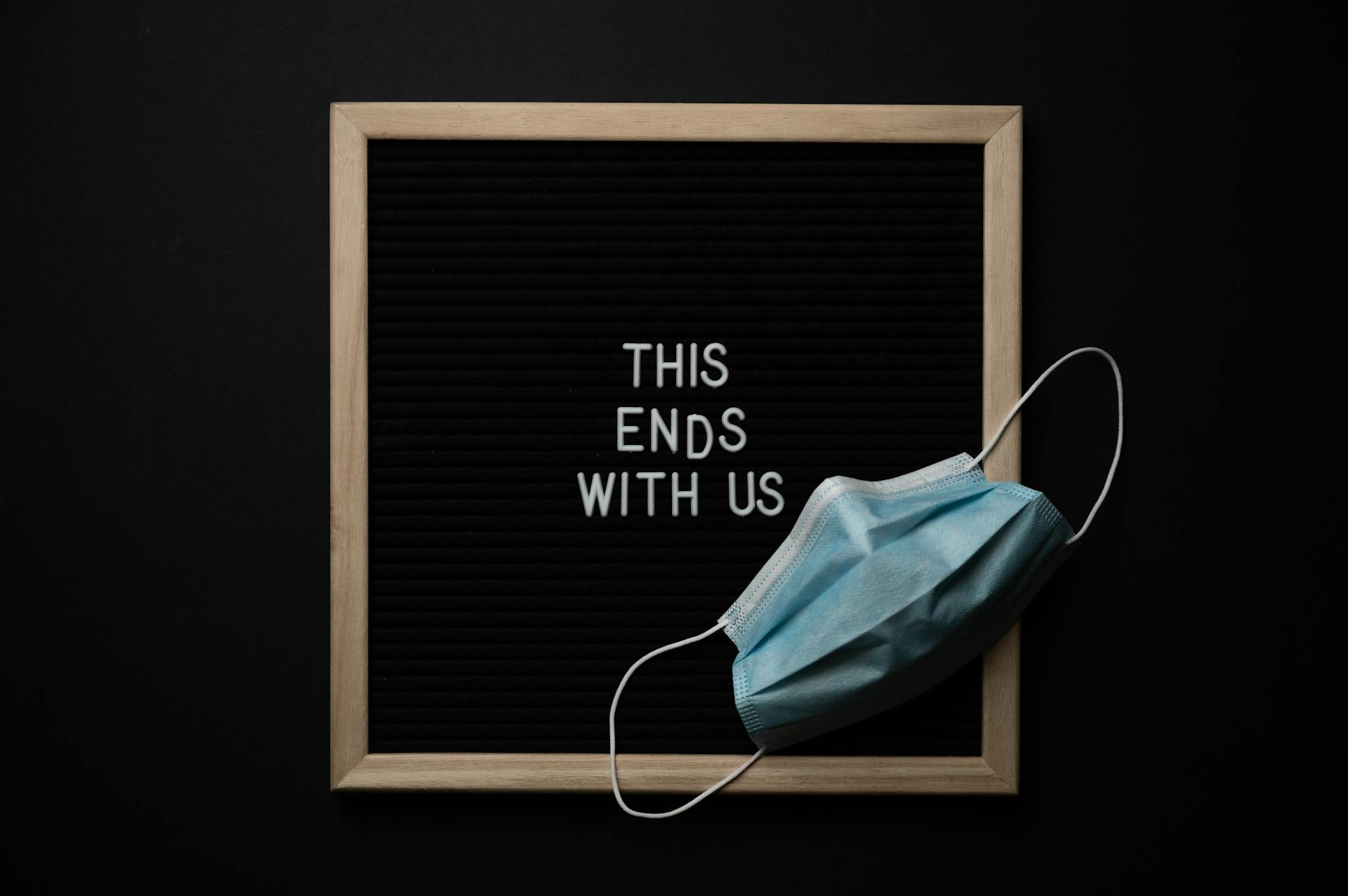 From above composition of sterile mask and black chalkboard with THIS ENDS WITH US inscription on black background