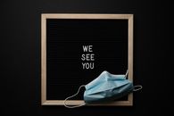 From above blackboard in wooden frame with white text on center under medical mask against black background