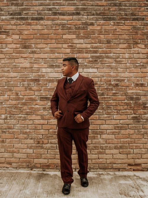 Free Full body adult male model in trendy brown suit standing at brick wall and looking away Stock Photo