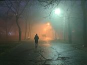 雾蒙蒙的公园小路上，路灯照亮着，一个人走着，捕捉到了神秘的夜景