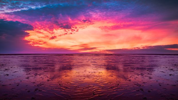 Dramatic sunset with vibrant colors reflecting on a tranquil ocean surface, creating a serene seascape.