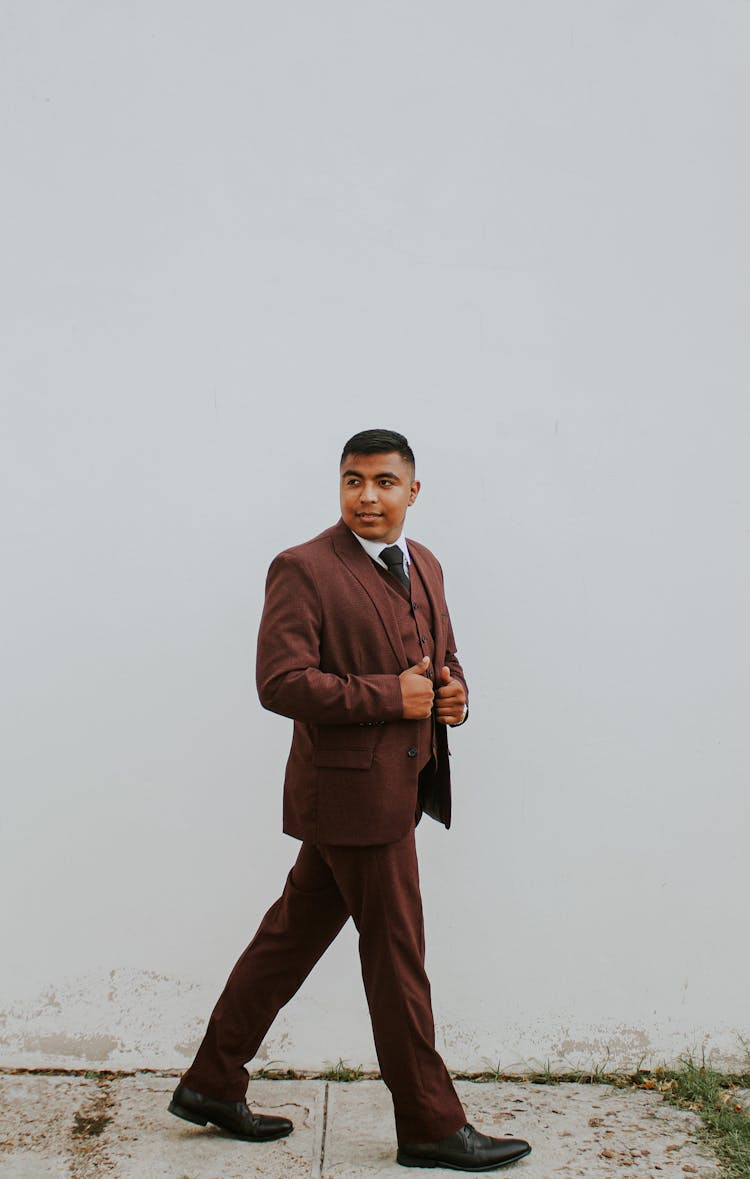 Elegant Ethnic Man In Suit Walking Alongside White Wall