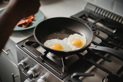Close-up of two fried eggs cooking in a frying pan on a modern stovetop.