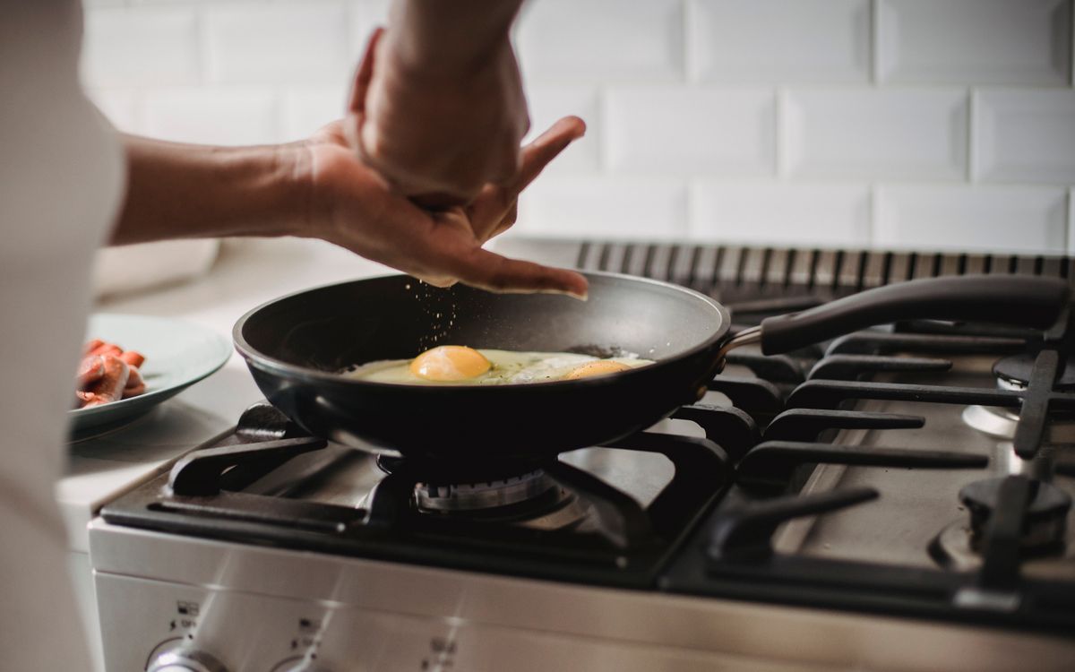Close-up of frying eggs on a gas stove with hands seasoning the dish.