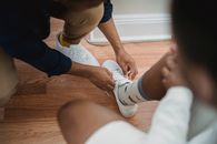 Close-up of a person tying sneakers with colorful socks on a wooden floor.