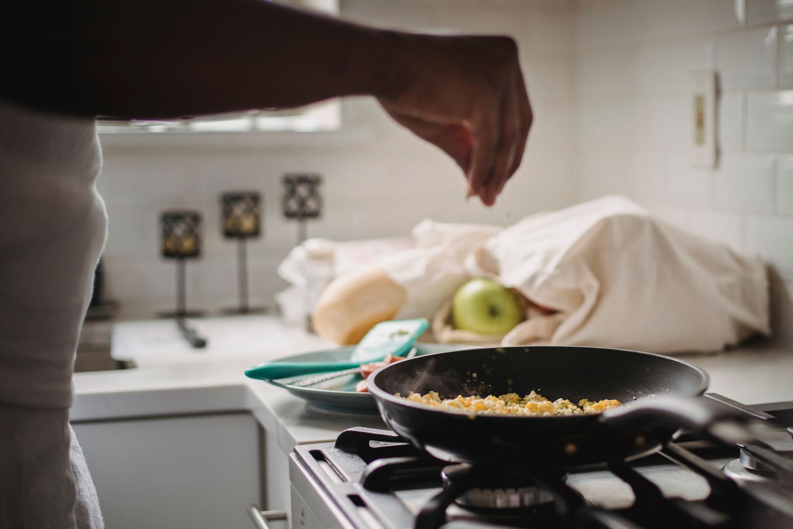 A person seasons scrambled eggs in a pan, capturing the art of home cooking.