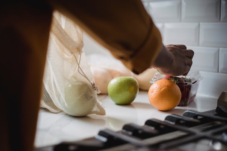 Person Unpacking Fruits On Kitchen Counter