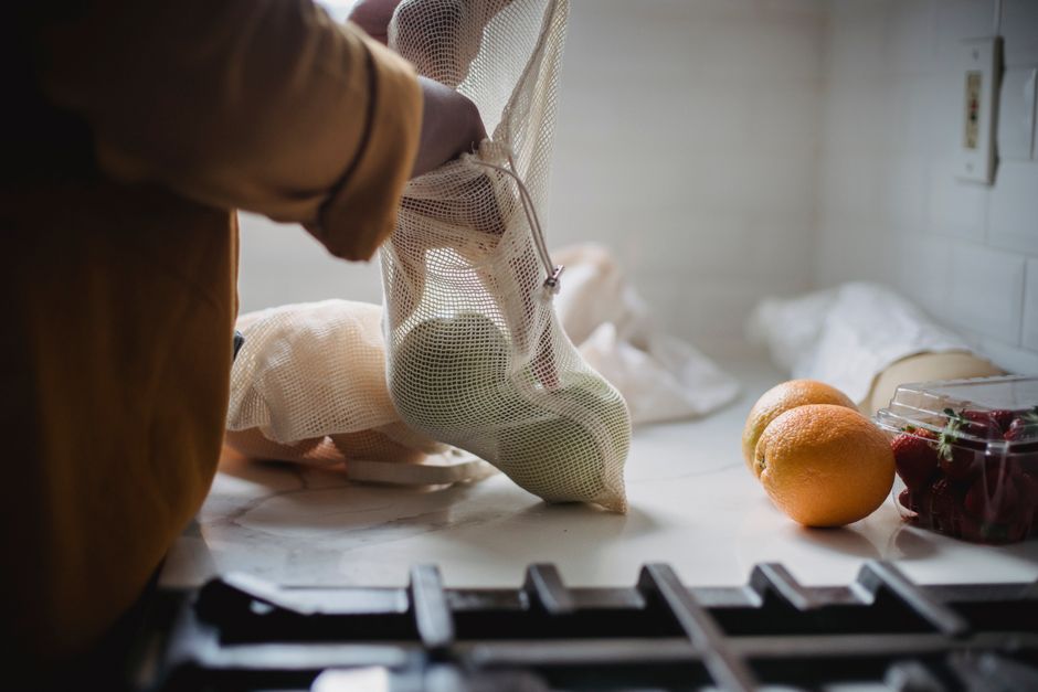 Hand placing fresh fruits in a mesh bag on a kitchen counter, promoting sustainability. - How to Reduce Everyday Household Plastic Waste Effortlessly
